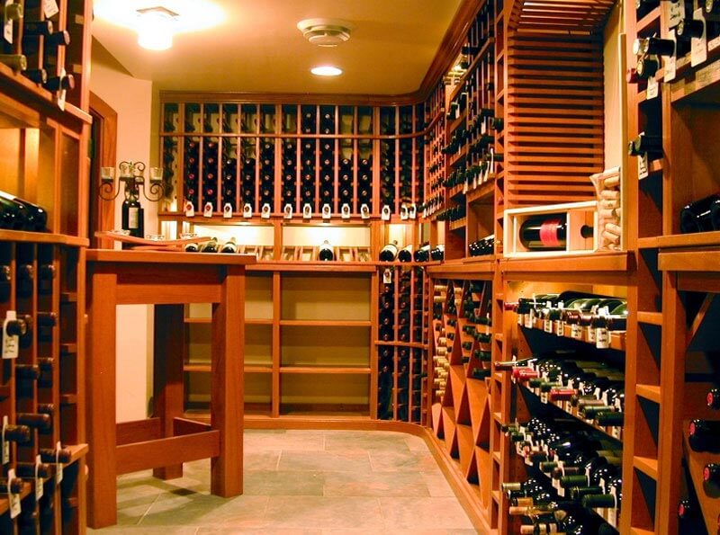 Individual wine racks with a LED lighted display row, solid rectangular and diamond bins, magnum cubbies and a 10-column soffit arch encircle the entire wine room providing ample storage for wine bottles of any size. A custom rustic Tuscan table provides additional storage and display opportunities to enjoy wine tasting inside the wine cellar.